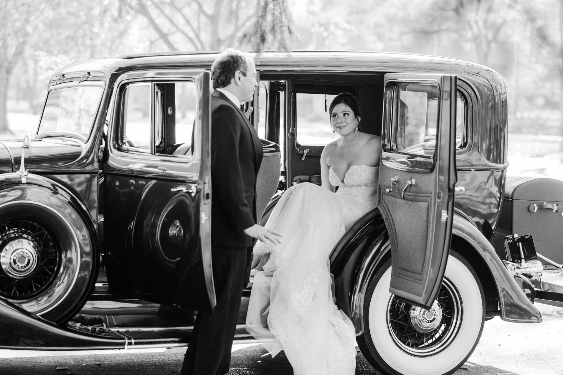 Bride getting into classic car on her wedding day.