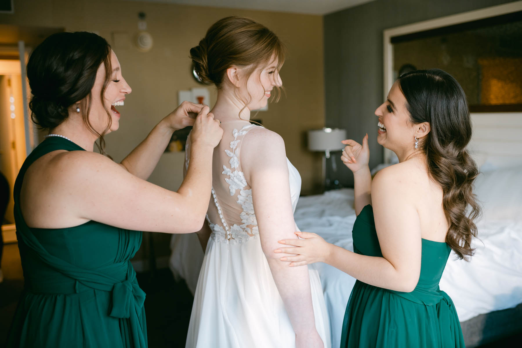 Bridesmaids in green helping bride get dressed.