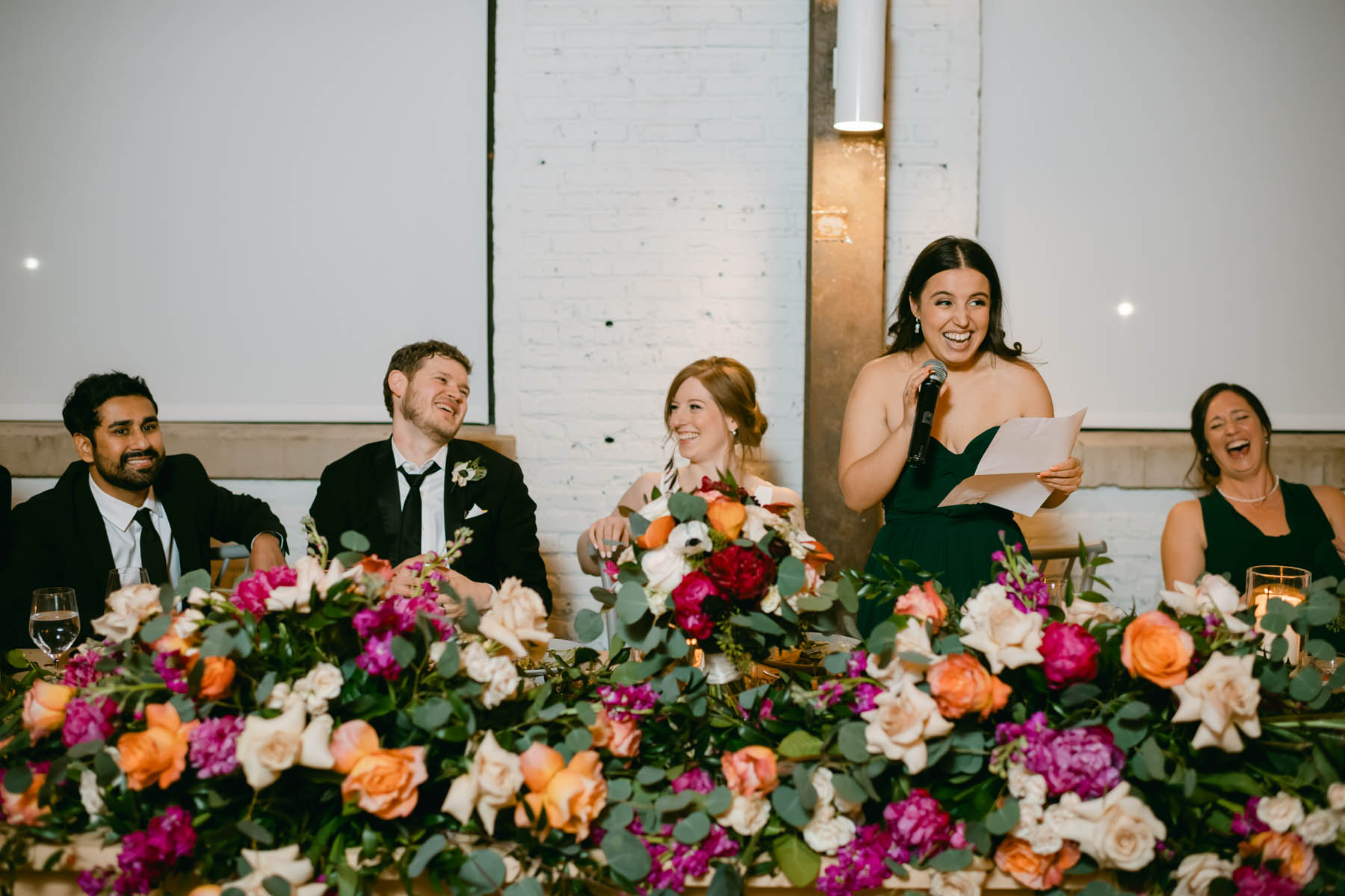 Maid of honor toasting wedding couple behind tropical flowers.