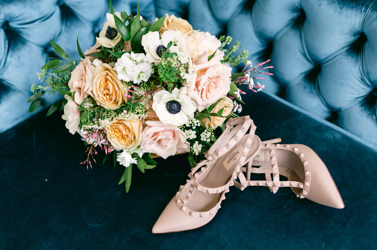 Wedding bouquet and shoes on blue couch.