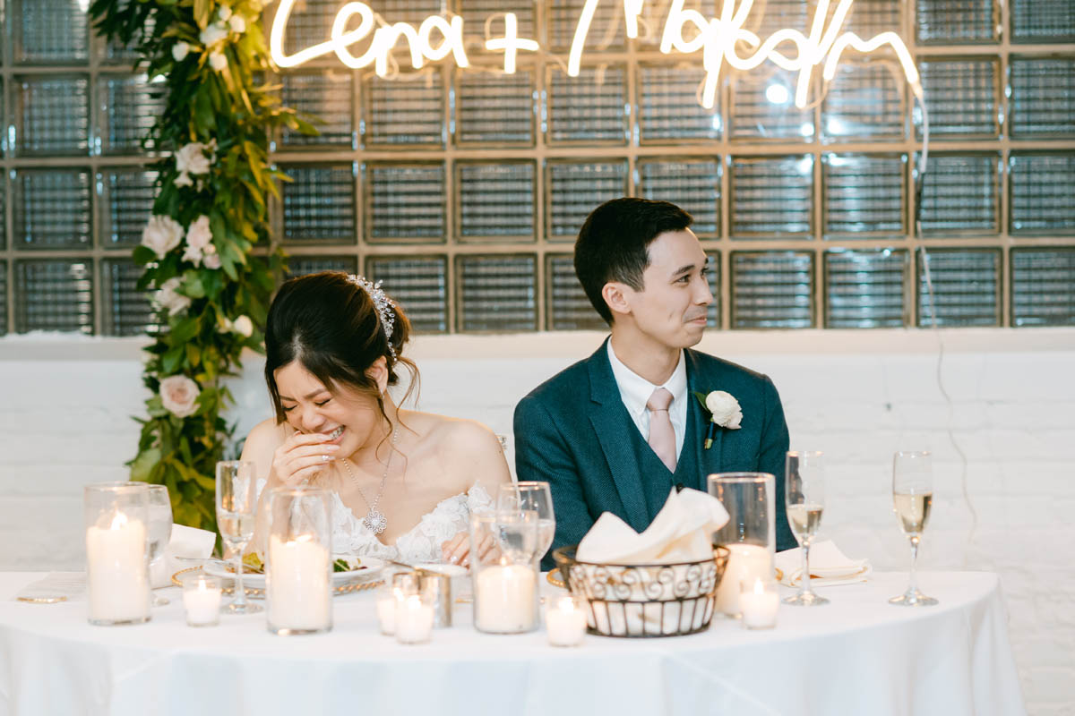 Bride and groom laugh during wedding toasts.