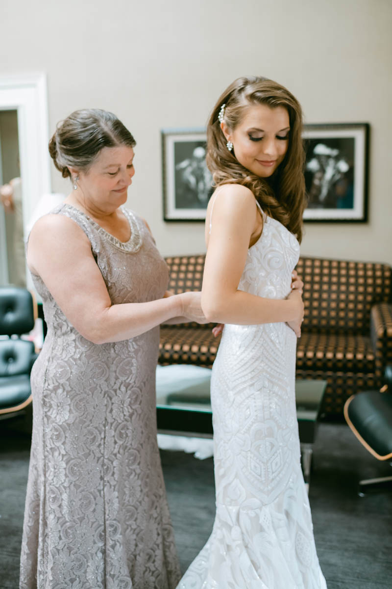 Mom smiling at bride getting into wedding dress.