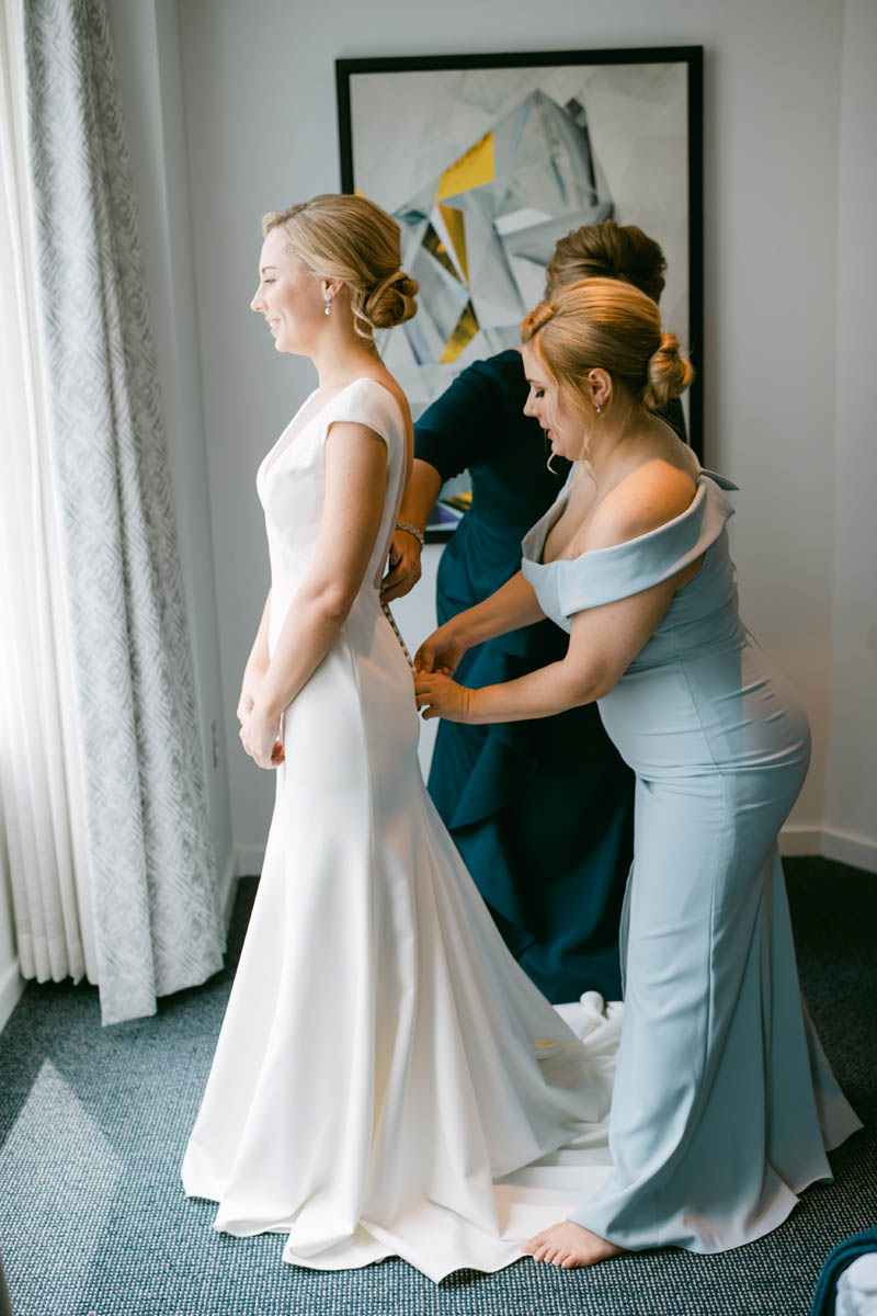 Bridesmaid helping bride into her wedding dress.