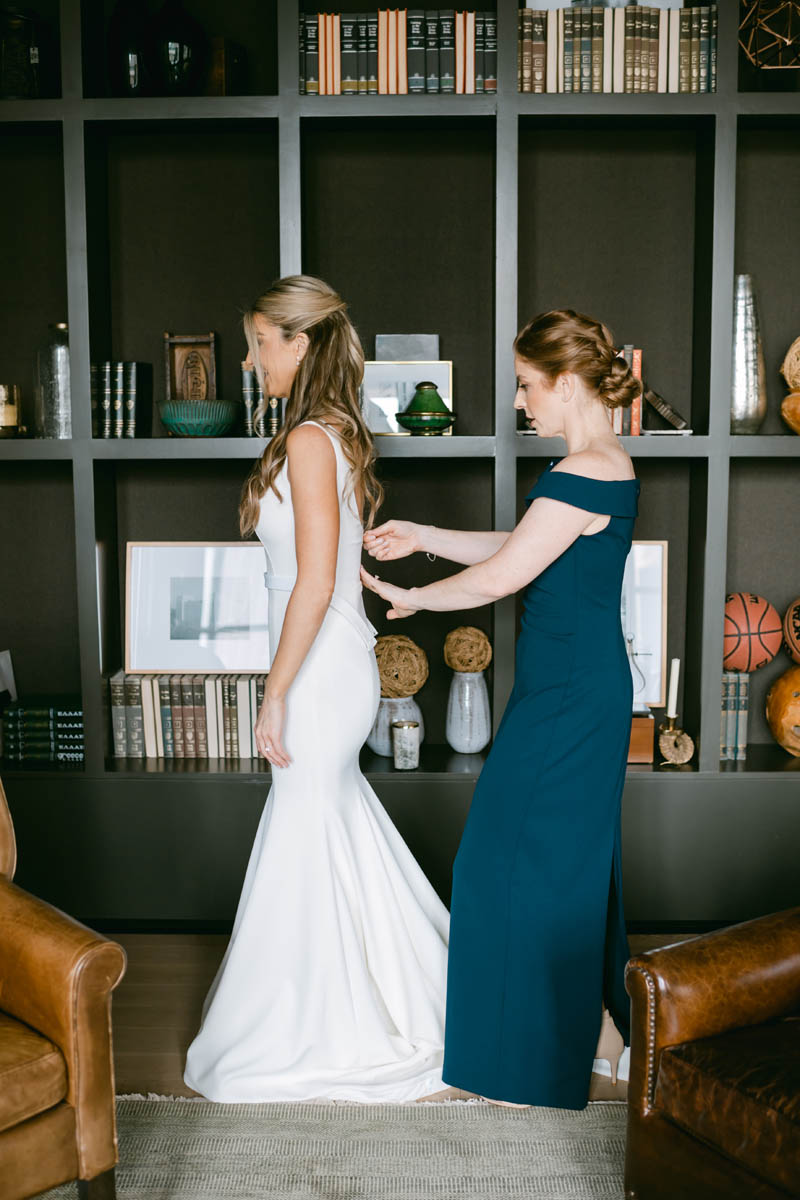 Maid of honor in blue dress helping bride get ready.