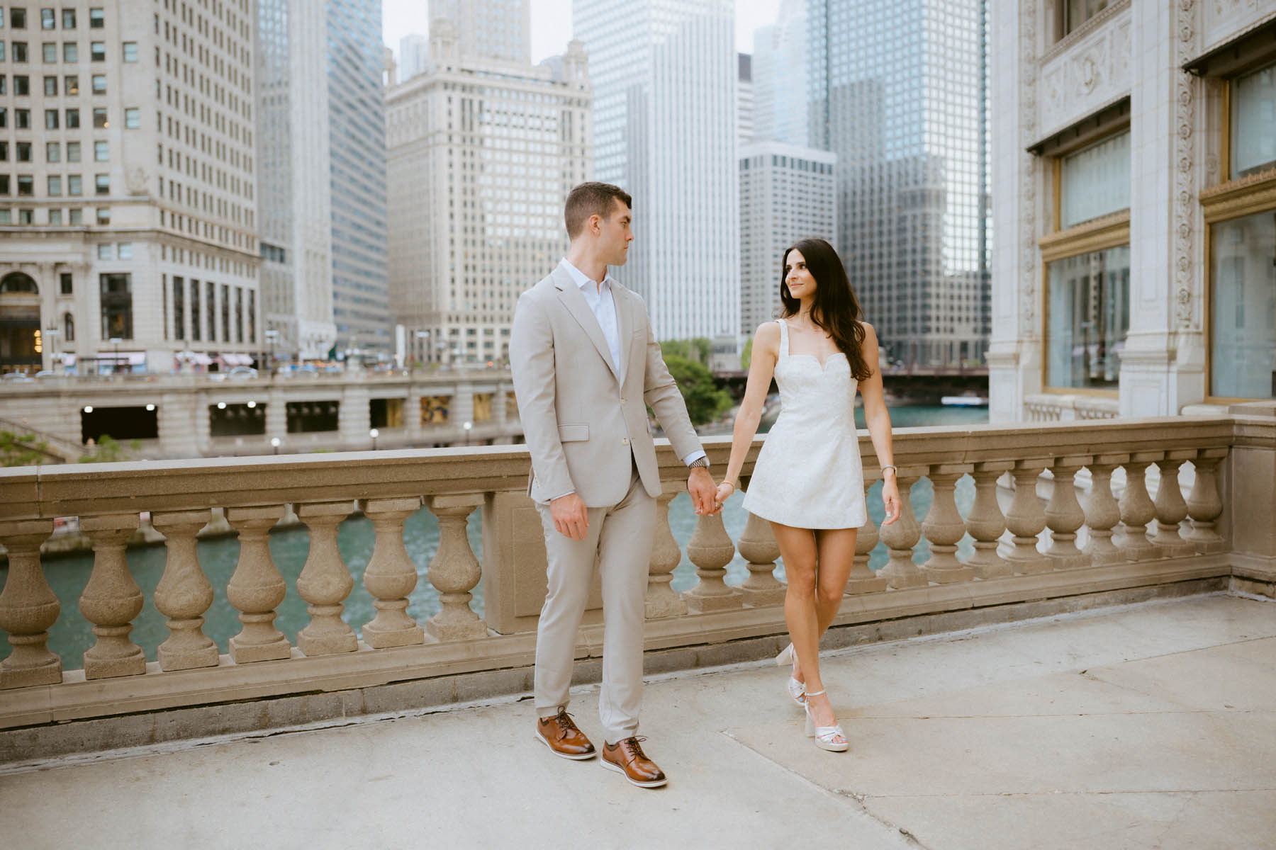 Romantic engagement portrait beside the Chicago River with city buildings softly blurred.