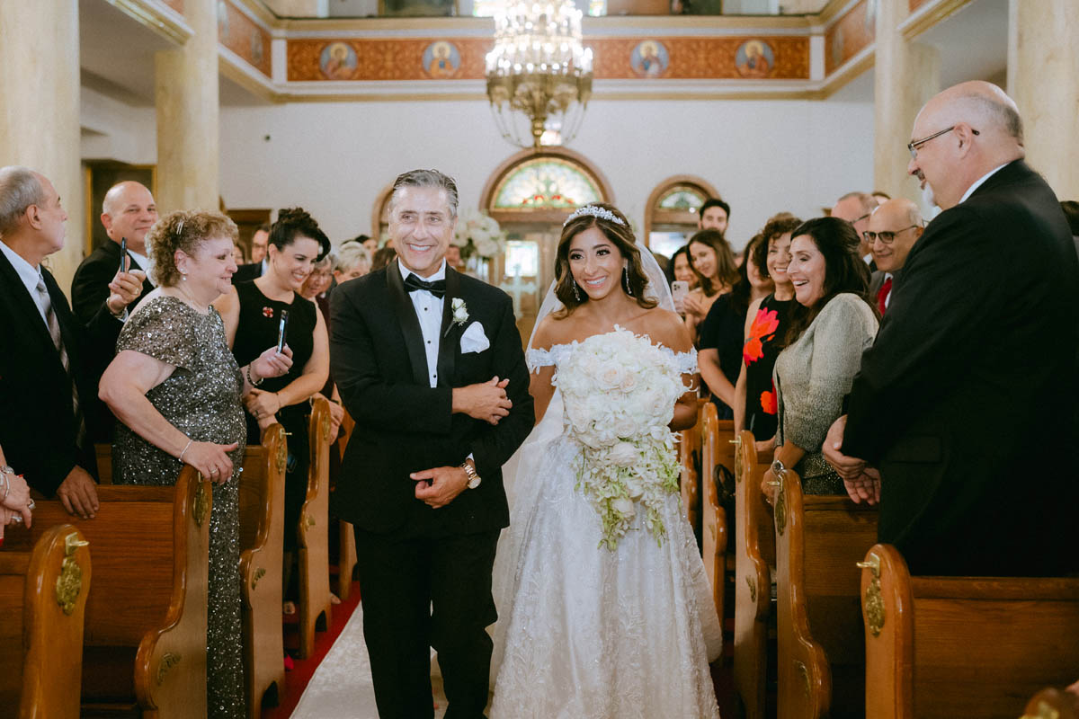 Smiling bride walking down the aisle with her dad at Annunciation Greek Orthodox Cathedral