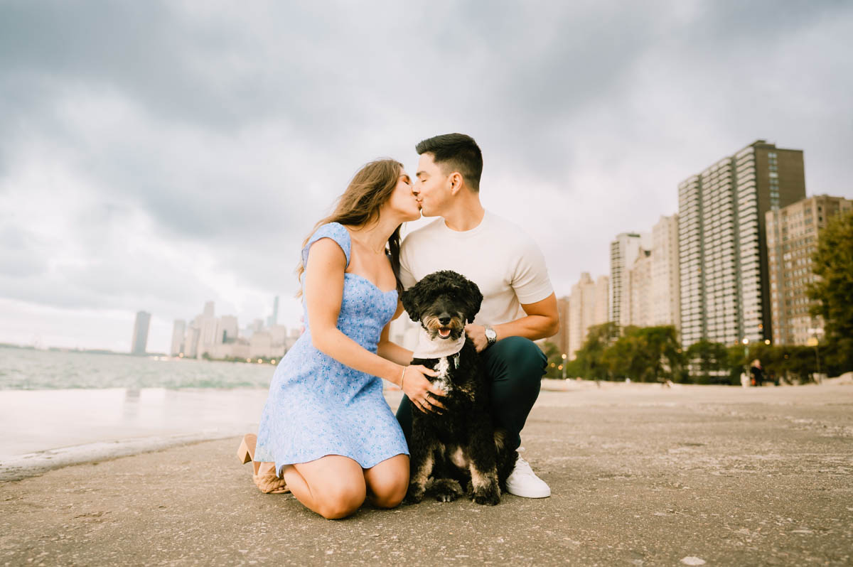 Chicago engagement photo of a couple sitting with their dog along the Lake Michigan shoreline with the Chicago skyline