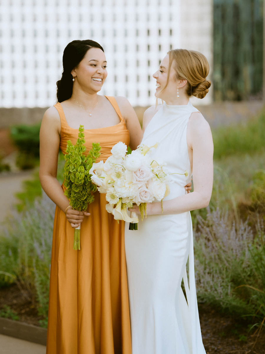 Bride and bridesmaid smiling together while holding the wedding bouquet