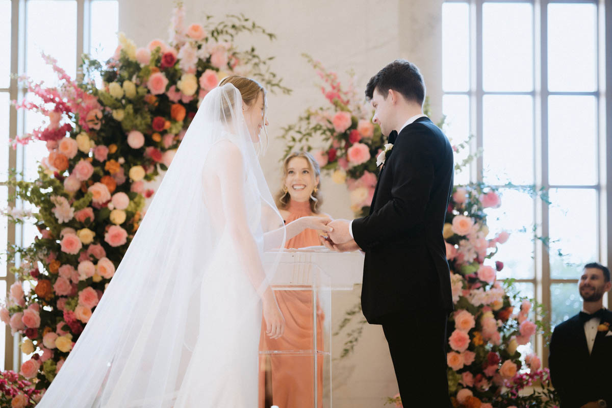 Bride and groom standing together beneath a floral wedding ceremony arch
