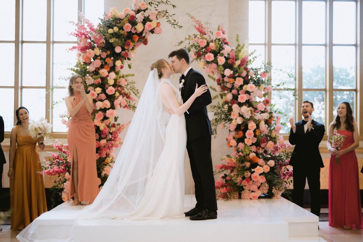Bride and groom sharing a kiss beneath a floral wedding ceremony arch