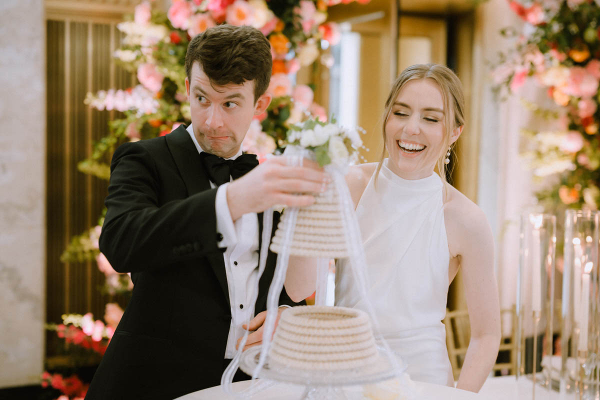 Bride and groom laughing together beside their wedding cake