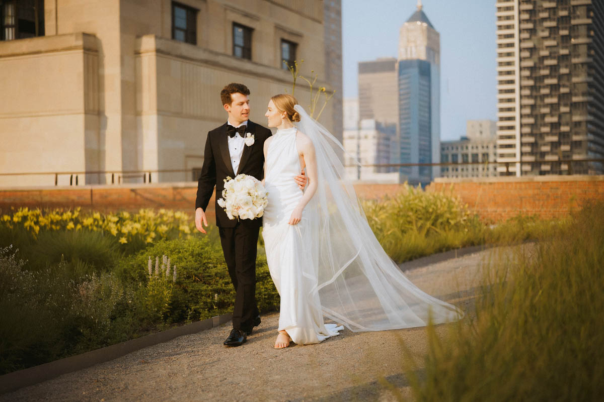 Bride and groom walking together on the rooftop with her wedding veil flowing